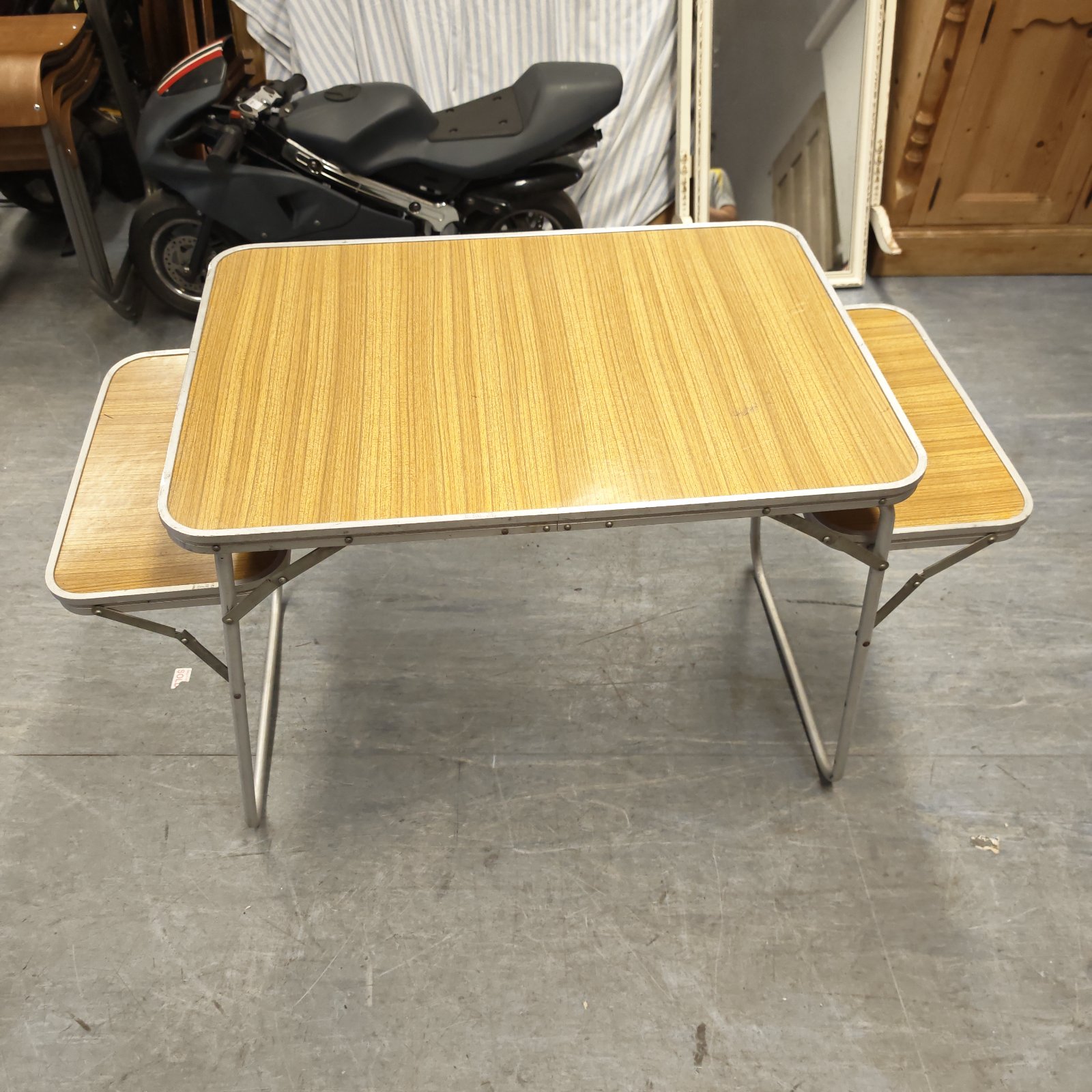 Vintage folding camping table with woodgrain top and metal legs.
