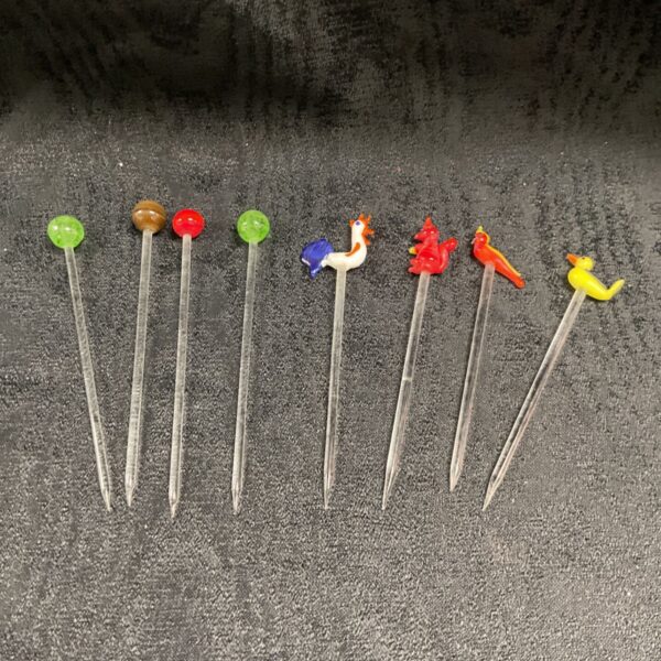 Eight vintage glass cocktail sticks with coloured heads and figural toppers on dark fabric