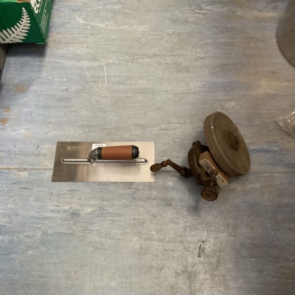 Vintage hand-crank bench grinder beside a stainless steel plastering trowel