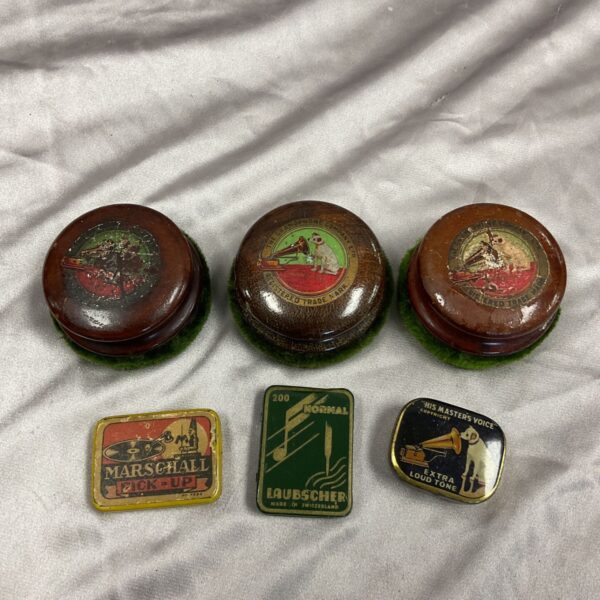 Three vintage HMV vinyl cleaning pads and three gramophone needle tins on a grey fabric background