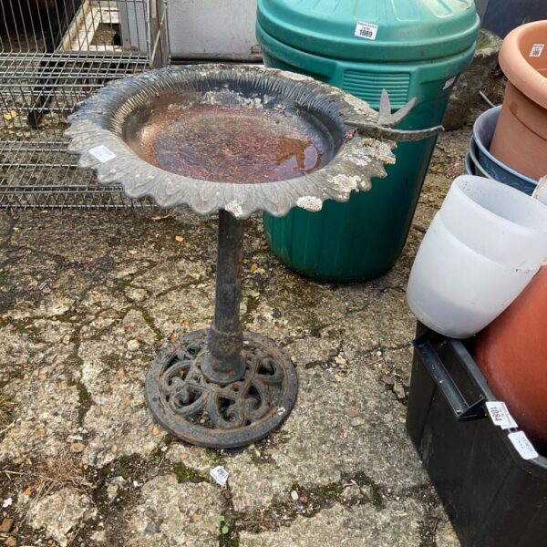 Vintage metal bird bath with cast iron base in a garden setting.