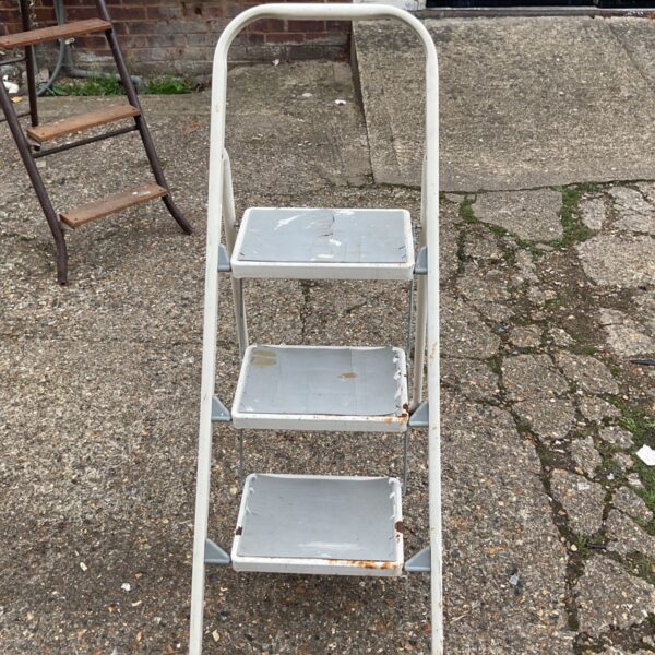 Vintage metal step ladder with three steps, showing signs of wear.