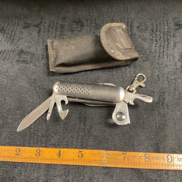 Vintage multi-tool pocket knife with magnifier and black nylon pouch on grey surface