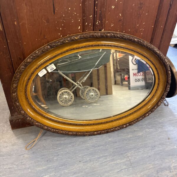 Vintage oval mirror with ornate carved wood frame and bevelled glass.
