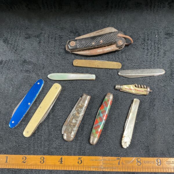 Ten assorted vintage pocket knives laid out on dark fabric with Rabone ruler