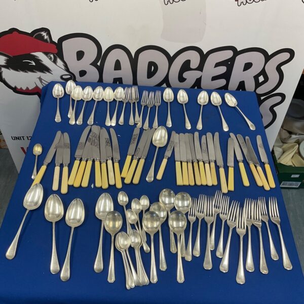 Vintage silver plated cutlery laid out on blue cloth, with spoons, forks and yellow handled knives