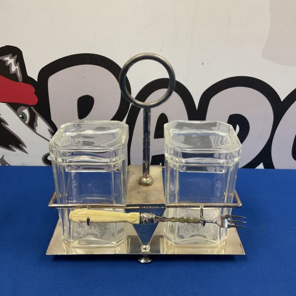 Vintage silver plated pickle jars with serving fork on display.