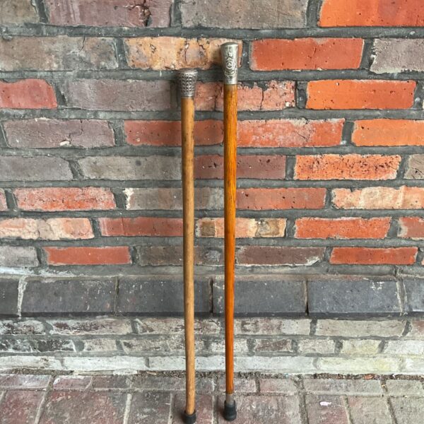 Pair of vintage silver topped walking sticks with wooden shafts standing against brick wall