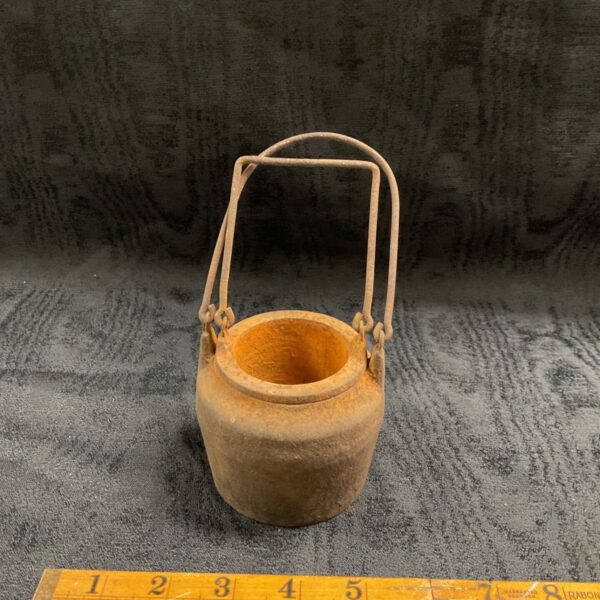 Small vintage cast iron gluepot with wire bail handle on grey fabric
