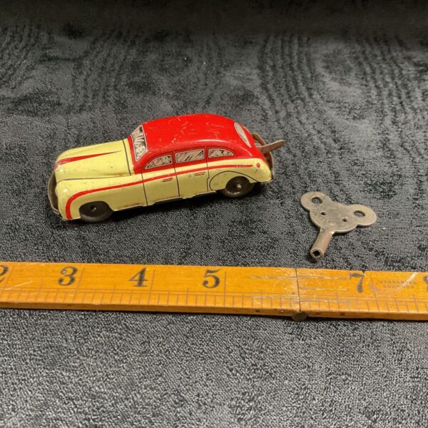 Vintage tinplate clockwork car with cream body and red roof beside a key