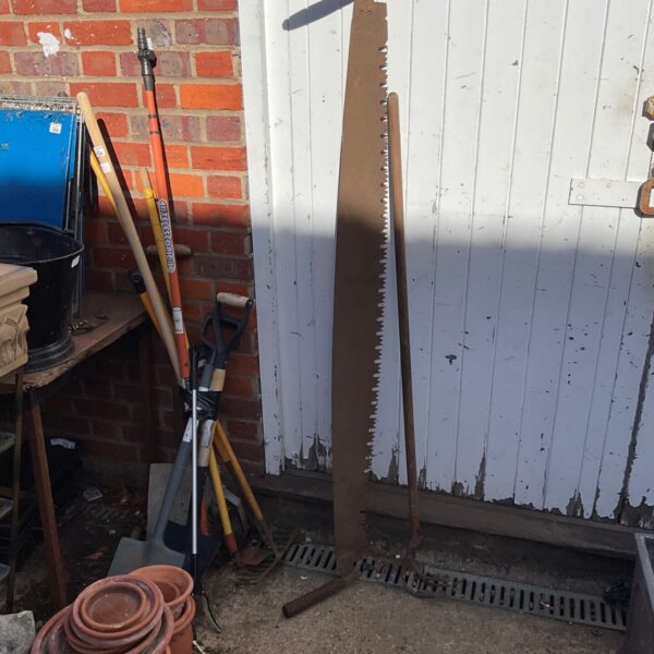 Antique two man saw and draw hoe leaning against a wall.