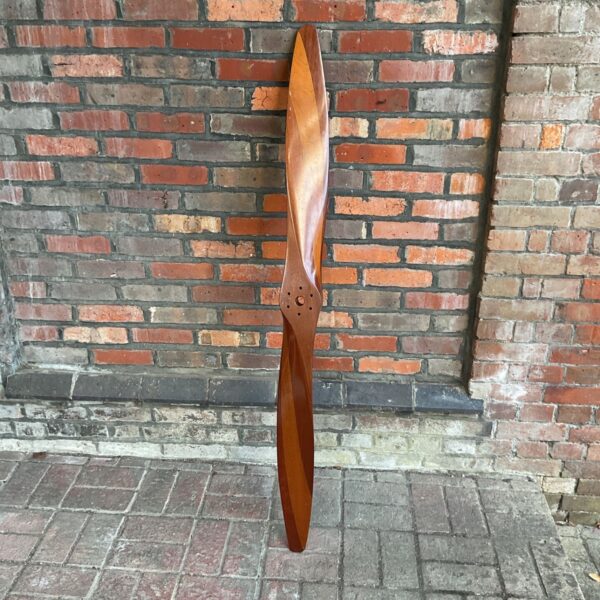 Vintage wooden airplane propeller against a brick wall.