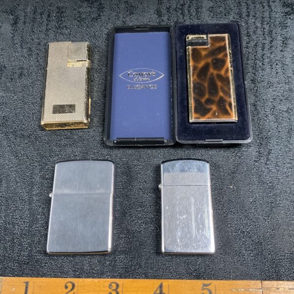 Four vintage pocket lighters with a Comoys Elegance case, shown beside a ruler