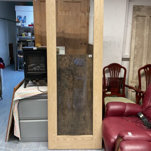 Pale wooden door with large glass panel, standing upright in a storage space