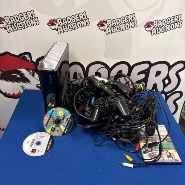 Xbox 360 console with tangled controllers, cables and PlayStation 2 games on blue table