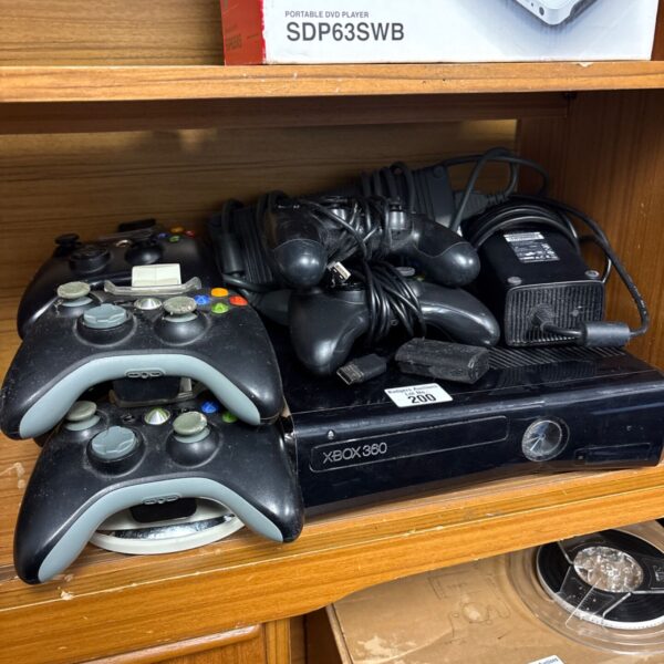 Black Xbox 360 console with controllers, power supply and cables on wooden shelf