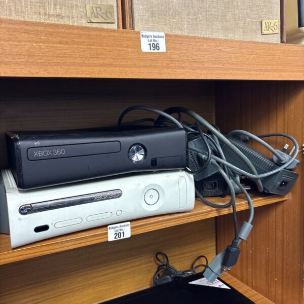 Two Xbox 360 consoles with power supplies and cables on shelf
