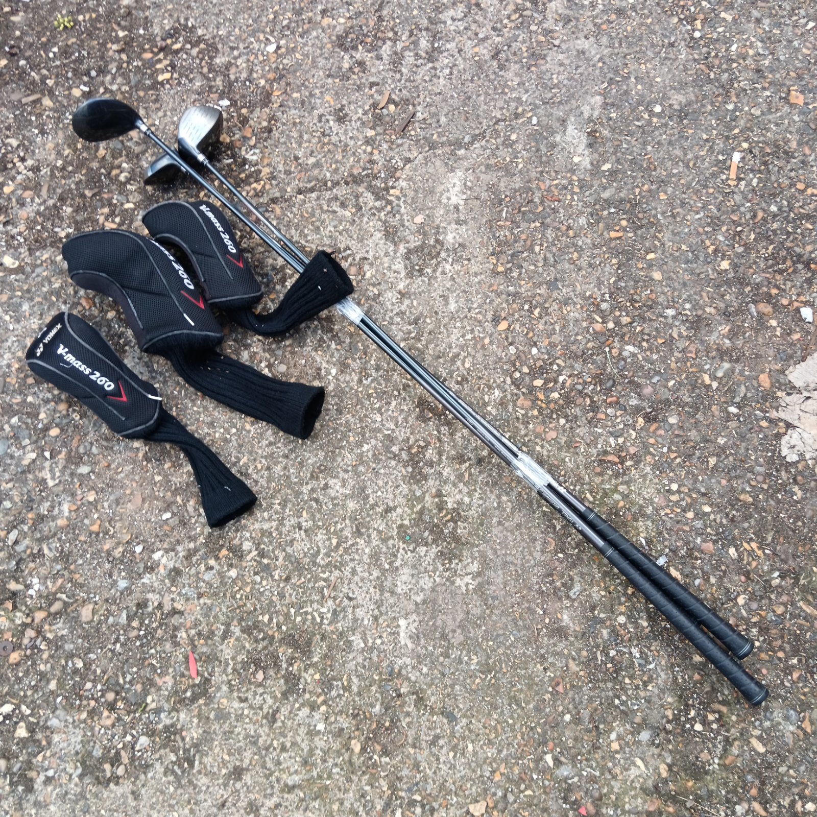 Yonex golf clubs with headcovers on a concrete surface.